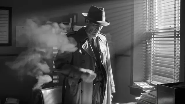 Black and white film noir frame: a detective in a trench coat and hat beside a window blind, smoke drifting